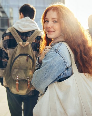 Rothaarige Studentin lächelt über ihre Schulter hinweg in die Kamera