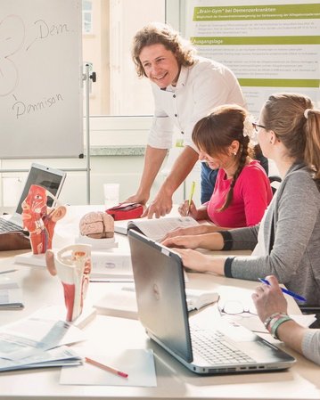 Dozent beugt sich über den Tisch und spricht mit Studierenden.